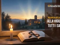 Preghiera della sera alla vigilia di Tutti i Santi Candela accesa con Bibbia aperta, rosario e crisantemi bianchi davanti a una finestra al tramonto, con una chiesetta illuminata sullo sfondo